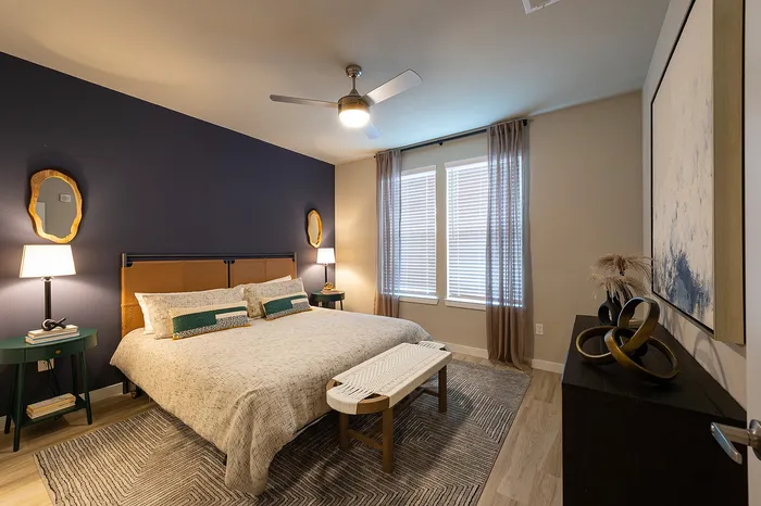 Modern bedroom featuring a cozy bed with stylish linens, ambient lighting, and elegant decor, highlighted by a rich navy accent wall.