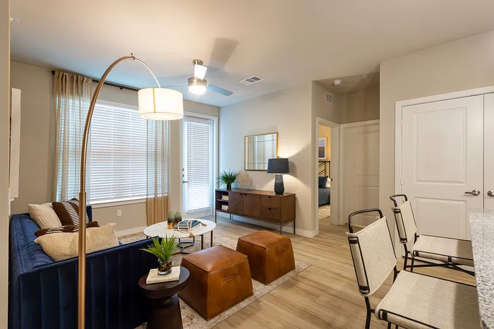 Inviting living space with contemporary decor, featuring a plush velvet sofa, elegant overhead lamp, and cozy seating area leading to a stylish bedroom.