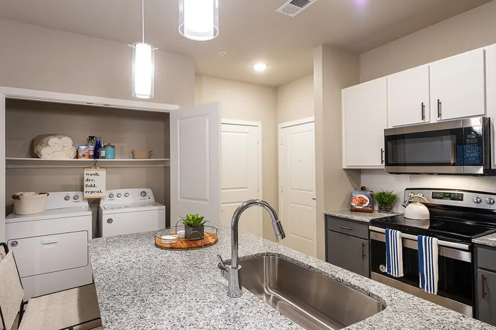 Modern kitchen with sleek granite countertops and stainless steel appliances, featuring a convenient in-unit laundry area.