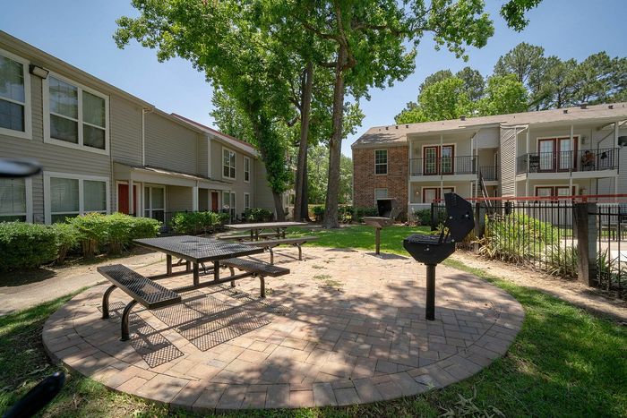 Inviting outdoor area with picnic tables and barbecue grills surrounded by lush greenery and modern apartment buildings.