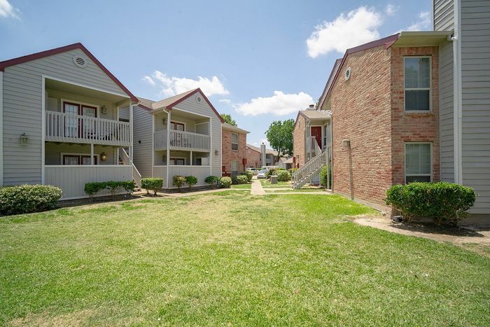 Charming apartment complex with inviting balconies, surrounded by lush green lawns and brick architecture under a clear blue sky.