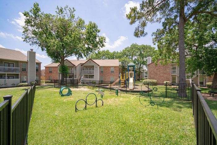 Charming apartment complex with lush green landscaping, a playful children's playground, and elegant balcony views.