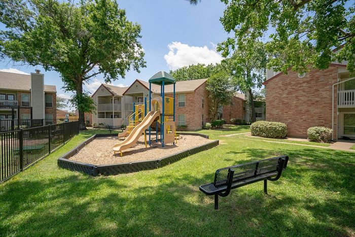 Charming apartment complex featuring a vibrant playground surrounded by lush greenery and modern brick buildings.
