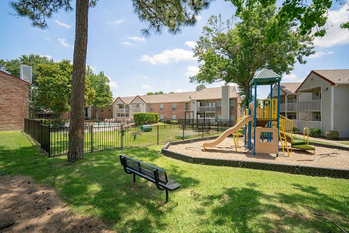 Charming apartment complex with landscaped greenery, a vibrant playground, and sparkling pool area, perfect for family-friendly living.