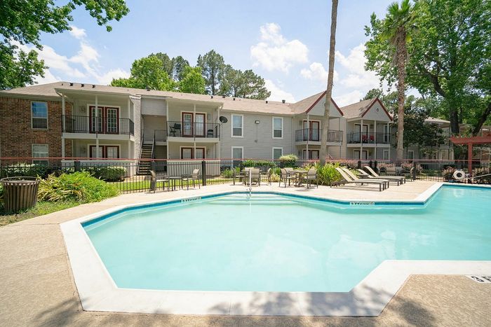 Inviting apartment complex featuring a glistening pool surrounded by lush greenery and sun loungers, perfect for relaxation and leisure.