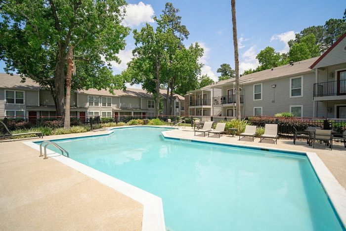 Inviting apartment community with a sparkling outdoor pool surrounded by lush greenery and relaxing lounge chairs.