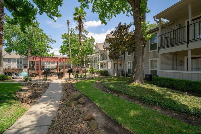 Charming apartment complex with lush landscaping, a shaded pergola, and modern amenities in a serene setting.