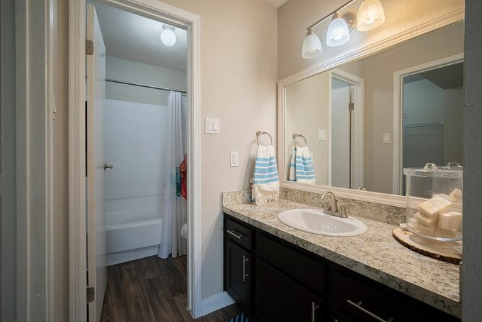 Modern bathroom with elegant granite countertop, stylish lighting, and inviting tub behind an open door.