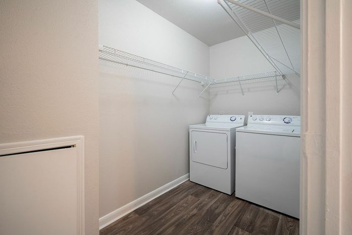 Modern laundry room with sleek hardwood floors, featuring a convenient washer and dryer set. Bright neutral walls and ample shelving for efficient storage.
