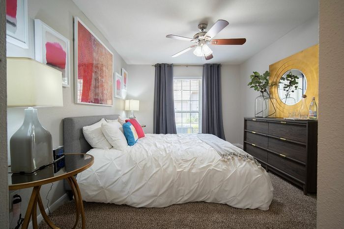 Cozy bedroom with elegant decor, modern ceiling fan, and abundant natural light pouring through a large window.