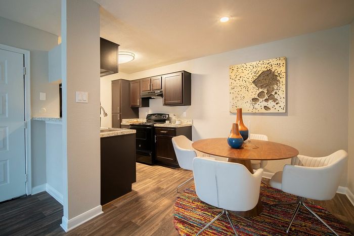 Contemporary dining area featuring a stylish round table with white chairs and vibrant decor, alongside a modern kitchen with dark wood cabinetry.