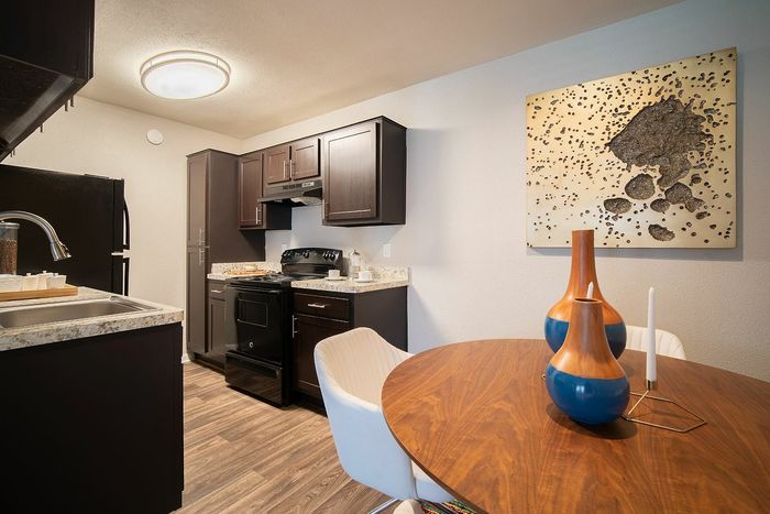 Chic kitchen and dining area featuring modern dark cabinets, elegant wooden decor, and stylish lighting above a cozy round table.