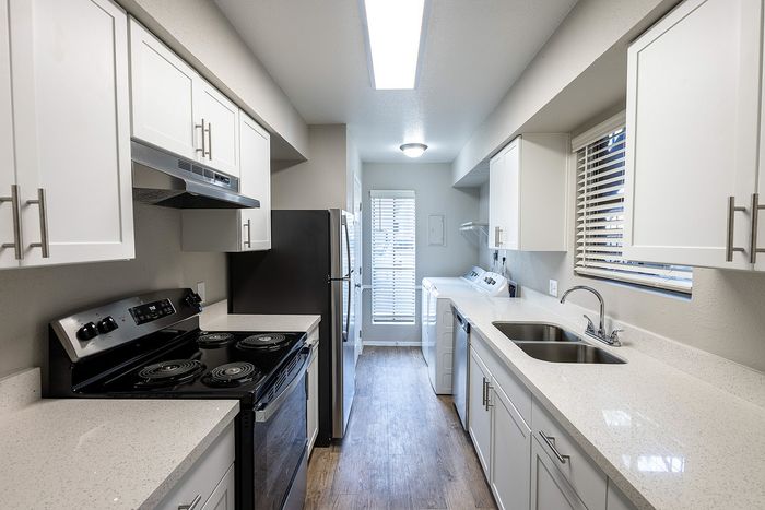 Modern galley kitchen with sleek white cabinetry, stainless steel appliances, and in-unit laundry for convenient urban living.