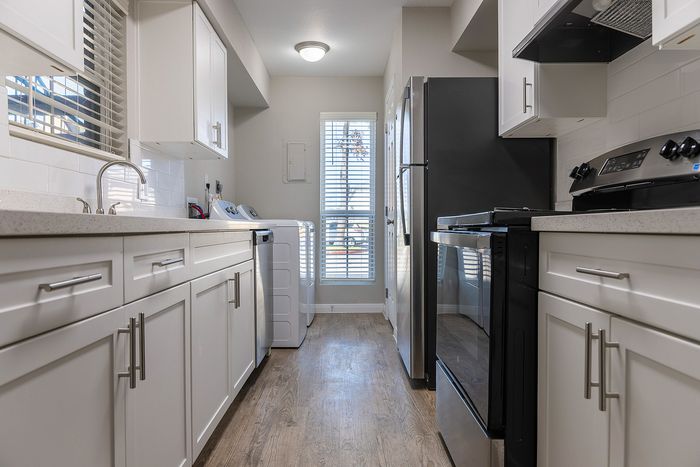 Modern kitchen with sleek white cabinetry, stainless steel appliances, and hardwood flooring, bathed in natural light.