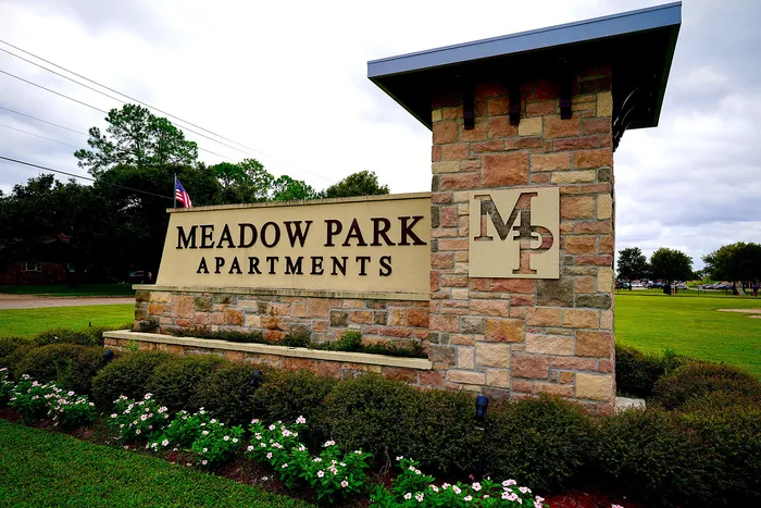 Inviting entrance sign for Meadow Park Apartments, surrounded by lush greenery and blooming flowers.