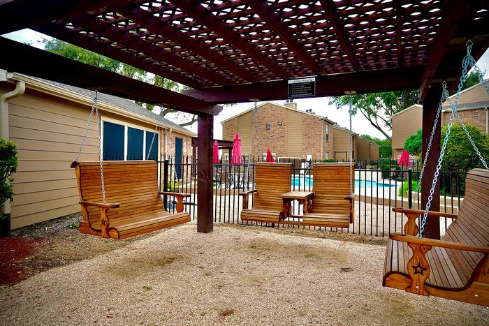 Inviting outdoor lounge with wooden swings under a pergola, offering a relaxing view of a sparkling pool surrounded by cozy seating and vibrant umbrellas.