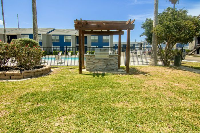 Inviting outdoor grill area with a wooden pergola and lush green lawn, overlooking a sparkling community pool for leisure and relaxation.