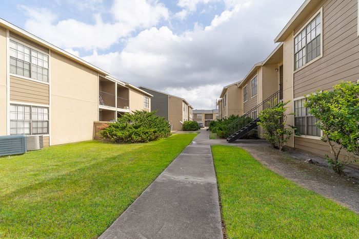 Charming apartment complex with well-maintained green lawns, surrounded by spacious balconies and modern architecture under a bright, inviting sky.