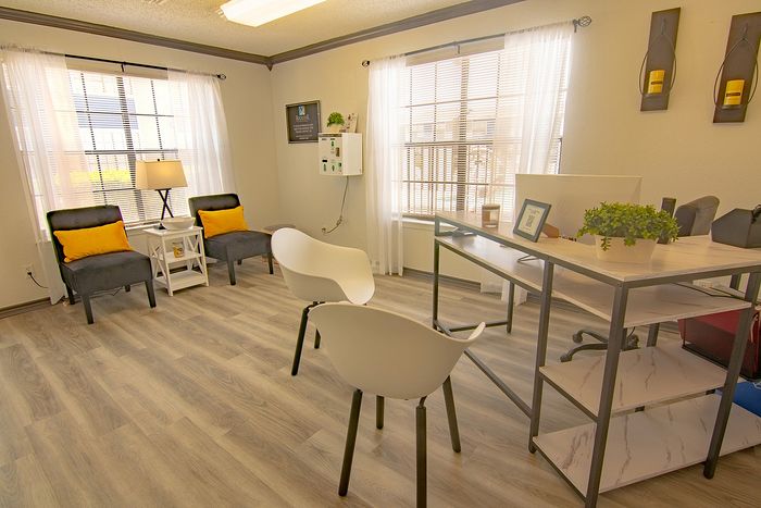 Inviting modern office space with natural light, featuring elegant wood flooring, cozy gray chairs with vibrant yellow pillows, and a sleek white desk adorned with greenery.