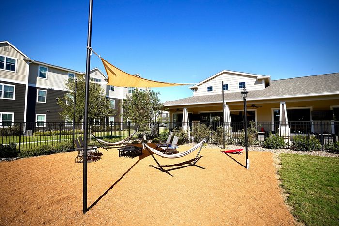 Sunny outdoor lounge area with hammocks and chairs in a modern apartment complex, complemented by lush greenery and a shaded sail. Perfect for relaxation and enjoying the serene environment.