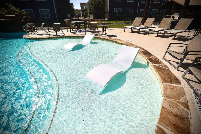 Luxurious poolside oasis with stylish in-water loungers and chic surrounding sun chairs.