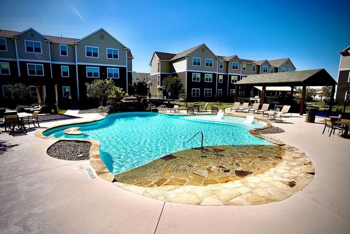 Luxurious apartment complex with a sparkling resort-style pool, surrounded by elegant lounge chairs and shaded seating areas, perfect for relaxation.