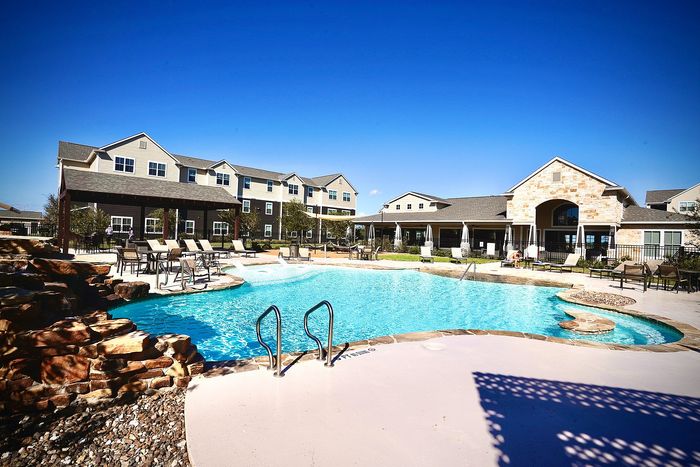 Inviting apartment complex with a sparkling outdoor pool surrounded by comfortable lounge chairs and well-maintained landscaping under a clear blue sky.