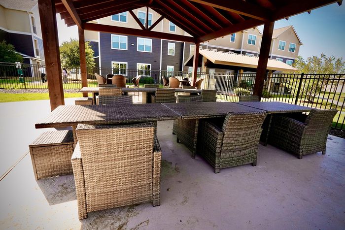 Charming outdoor patio with elegant wicker furniture and a view of modern apartment buildings, perfect for relaxation and social gatherings.