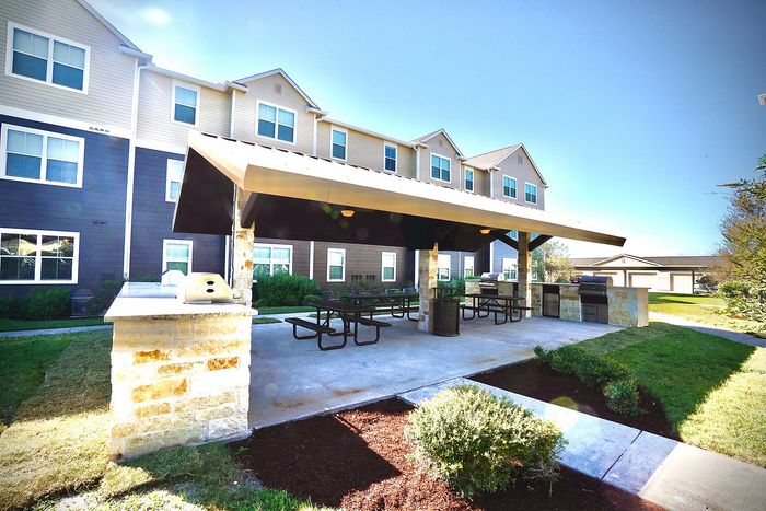 Charming outdoor communal area with covered seating, barbecue grills, and lush landscaping, perfect for gatherings and relaxation.