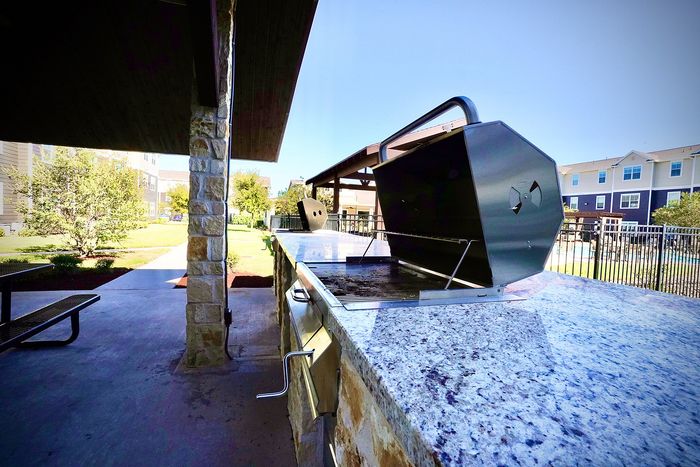 Elegant outdoor patio featuring a modern grill station with spacious countertops, surrounded by lush landscaping and upscale apartment views.