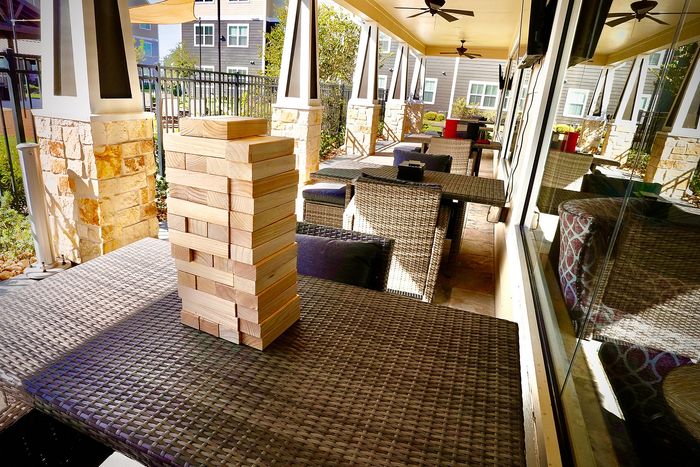 Inviting outdoor area with elegant wicker furniture and a fun wooden block game, perfect for social gatherings in a stylish apartment complex.