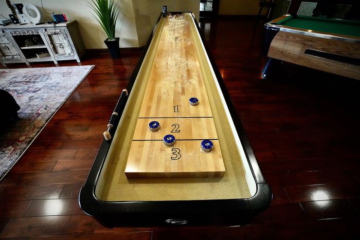 Luxurious apartment game room with a sleek shuffleboard table on polished hardwood floors, perfect for entertainment and relaxation.