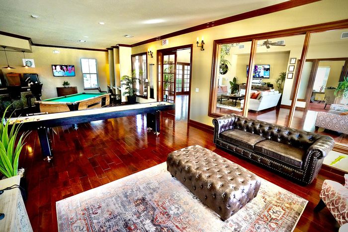 Elegant and spacious apartment interior featuring a chic leather sofa, stylish ottoman, and engaging game room with a pool table.