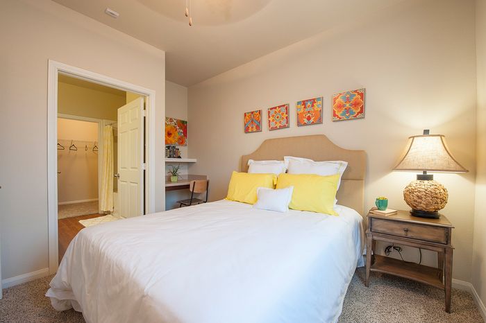 Inviting bedroom with plush bedding, vibrant artwork, cozy lighting, and a practical workspace, leading to a spacious walk-in closet.