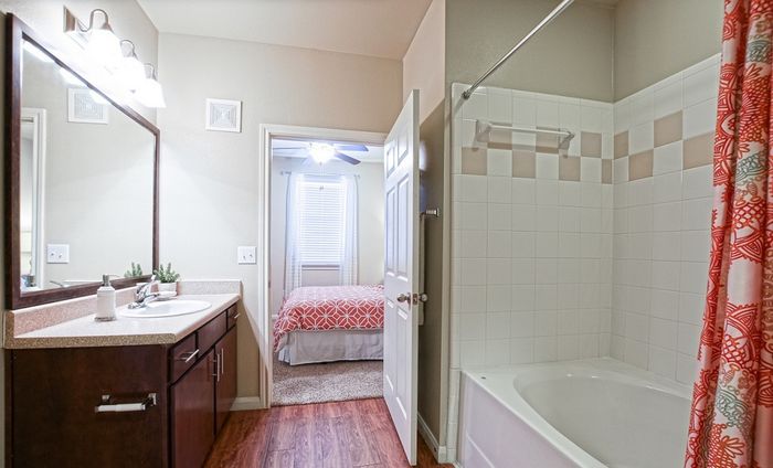 Inviting bathroom with modern fixtures, warm wood cabinetry, and a cozy view into a sunlit bedroom.