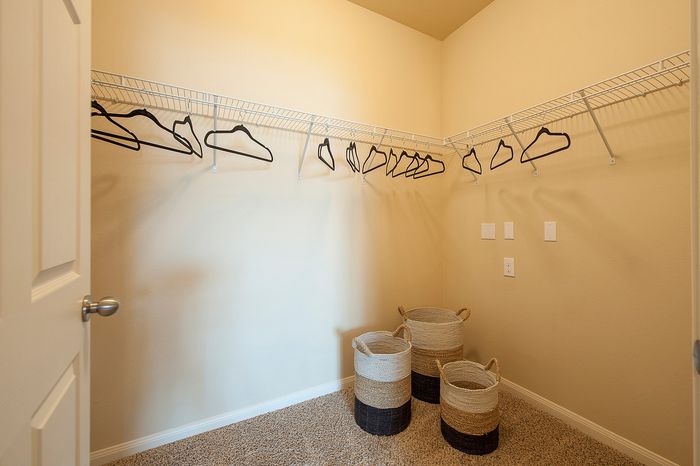 Spacious walk-in closet with elegant hanging racks and stylish woven baskets on plush carpet.