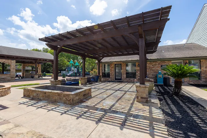 Charming outdoor space with a wooden pergola and cozy seating area, adjacent to a playful children's playground and a rustic community building.