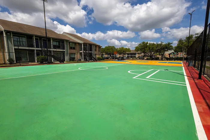 Bright and inviting apartment complex featuring a vibrant outdoor sports court under a sunny sky.
