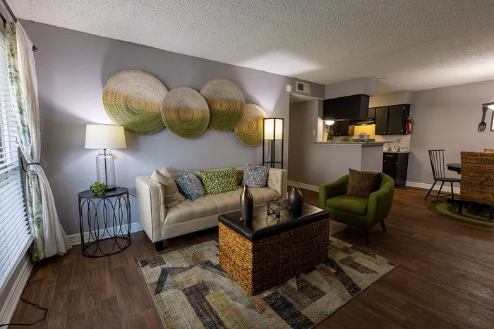 Inviting living area with stylish decor, featuring a cream sofa, green accent chair, and modern art, leading to an open kitchen with elegant furnishing.