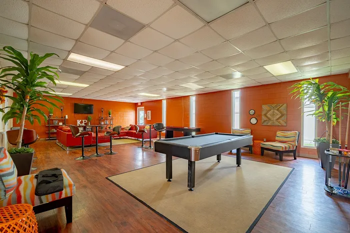 Vibrant recreational room featuring a stylish pool table, cozy red seating area, and modern decor with lush greenery.