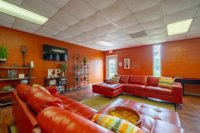 Vibrant community lounge featuring bold red leather sofas, modern shelving with decor, and a wall-mounted TV for a cozy living experience.