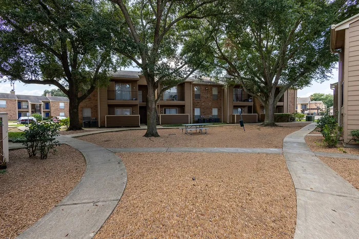 Charming apartment exterior surrounded by lush trees and serene walkways, offering a peaceful community atmosphere.