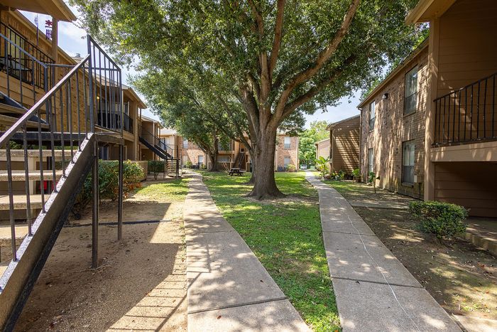 Charming apartment courtyard featuring lush greenery and shaded pathways amidst attractive brick buildings.