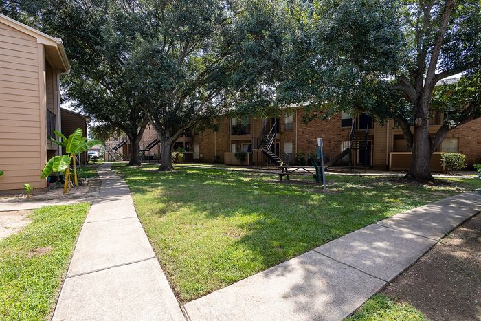 Charming apartment exterior with lush green spaces, shaded walkways, and outdoor seating for relaxation.