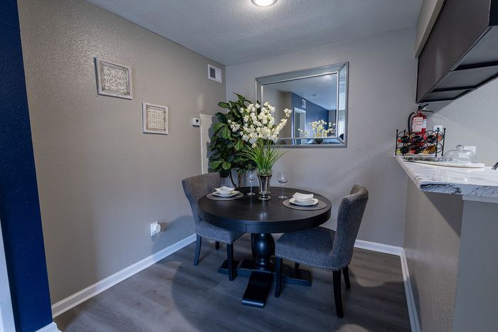 Charming dining nook with elegant table setting, stylish gray chairs, and a lush plant enhancing a cozy apartment ambiance.