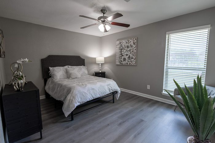 Inviting bedroom with elegant decor, featuring a plush bed, modern ceiling fan, and large window with natural light.