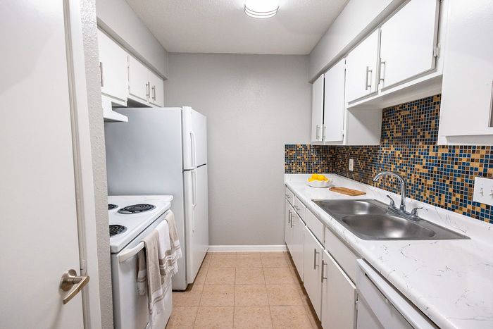 Galley-style kitchen at Huntington Oaks Apartments in Alvin, TX with white cabinetry and mosaic backsplash.