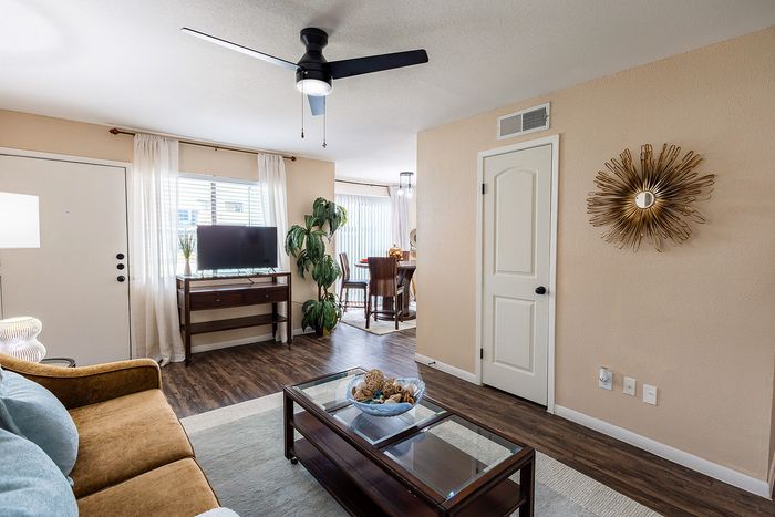 Bright and cozy living room with modern decor, featuring a plush sofa, stylish coffee table, and a sleek TV stand. Natural light streams through large windows, highlighting the inviting dining area in the background.