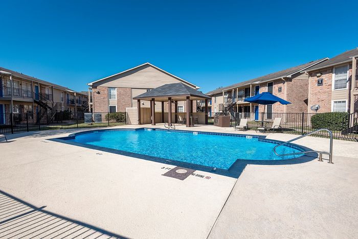 Swimming pool with shaded seating and apartment buildings at Steeplechase Apartments in Alvin TX