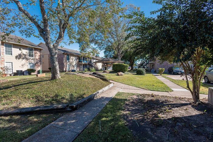 Community green space with trees and walking paths at Steeplechase Apartments in Alvin TX